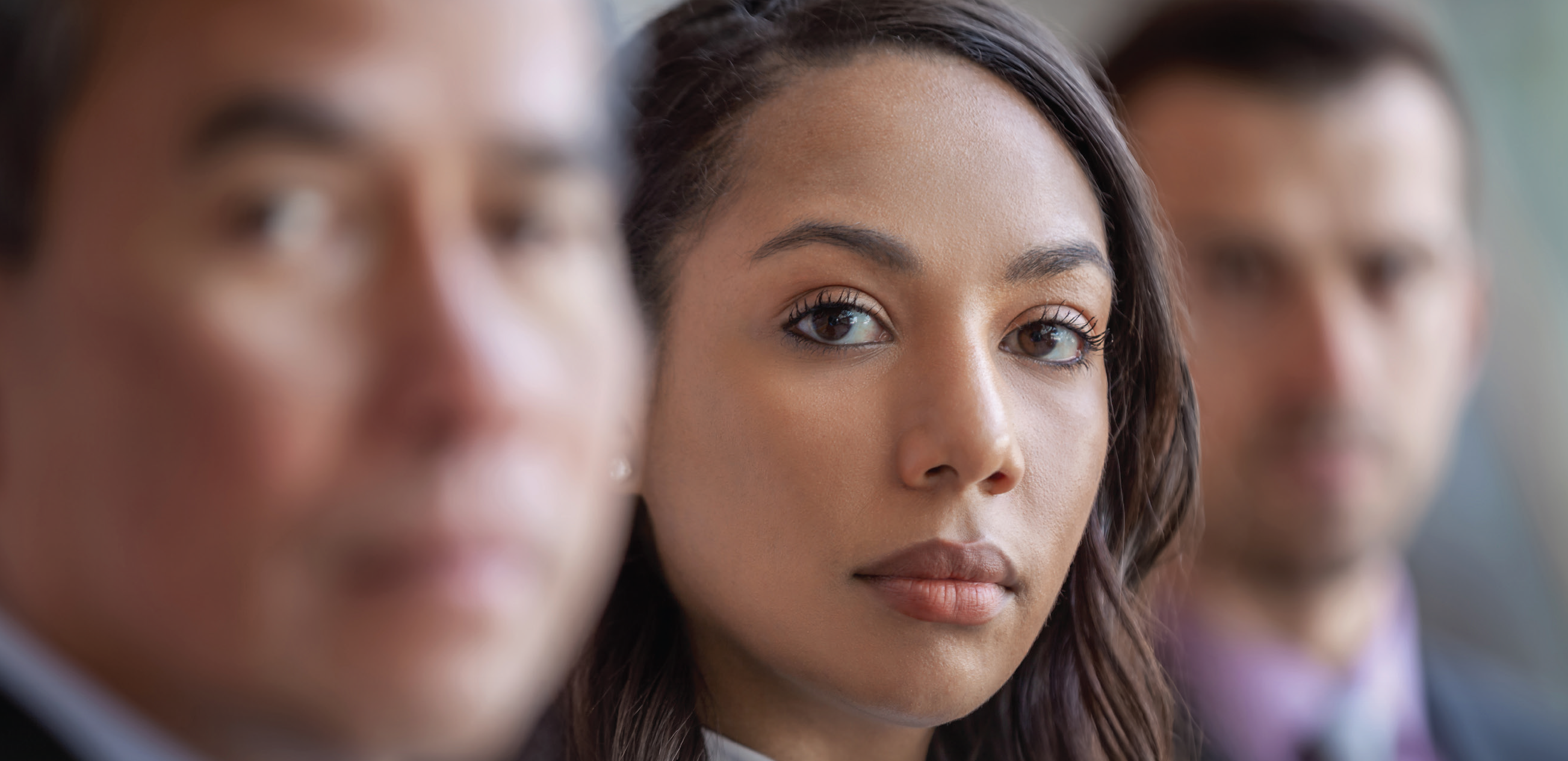 business woman looking directly into camera with faded out businessmen beside her