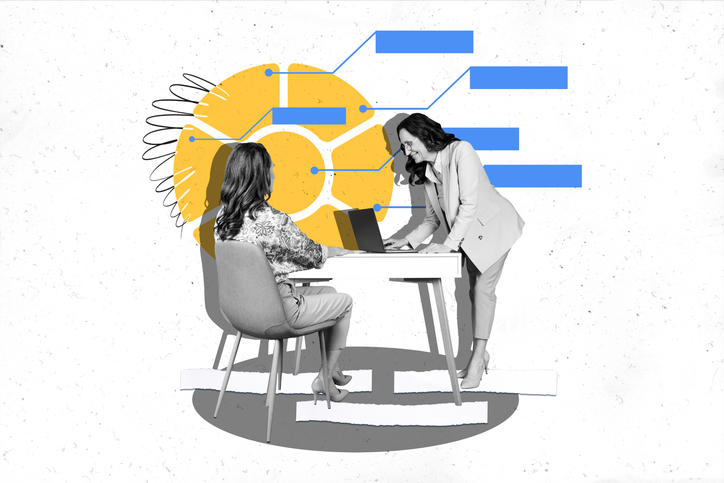 two women at computers smiling, one mentoring the other