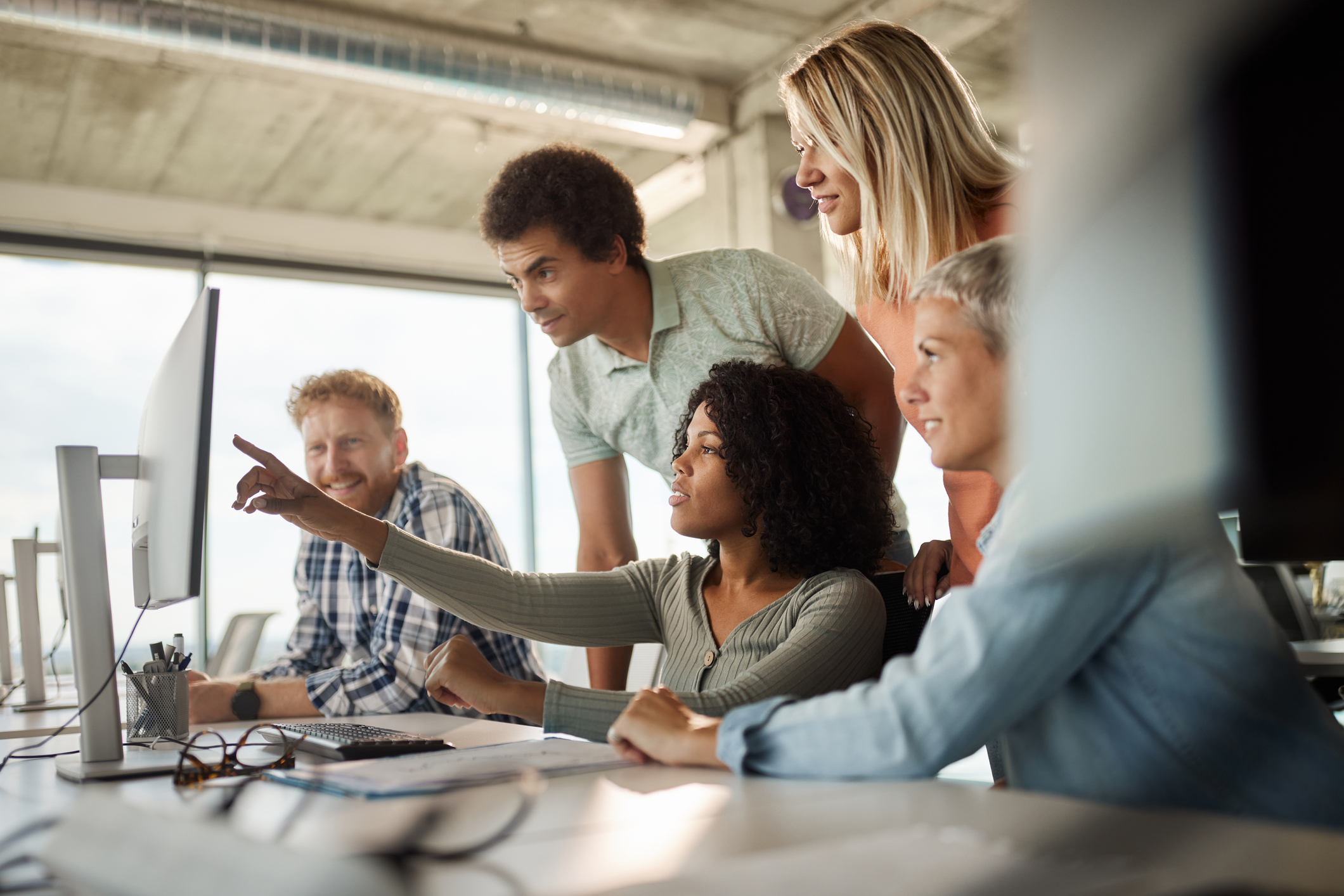 A group of five business people looking at a computer together at an agency, collaborating on the design of insurance agency websites and discussing the launch of a new website.