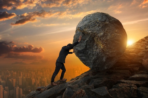 business man pushes large stone up hill