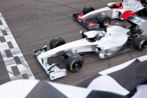 Race cars crossing the finish line with a checkered flag in view.