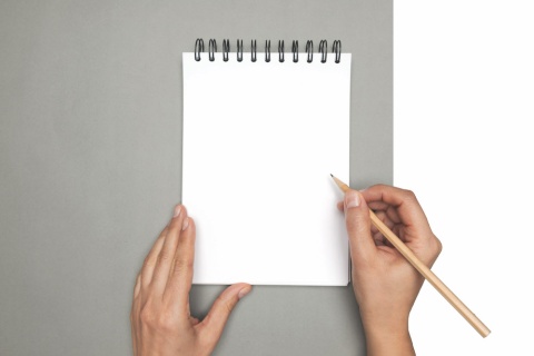 Pair of hands writing on a blank note pad.