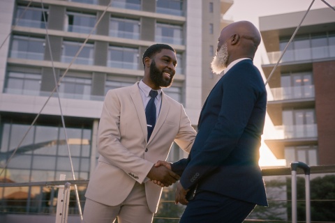 Two professionals shake hands in the city, forging connections within insurance cluster groups. Independent agencies collaborate to gain access to new opportunities and expand their reach.