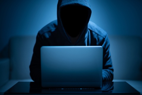 Hooded man with face covered working on a laptop to steal someone's identity