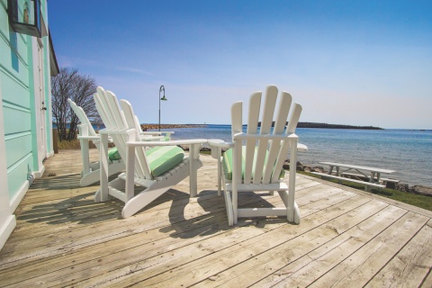 Adirondack chairs on a deck of a vacation home overlooking a lake. 