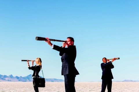 three people in a desert looking out with telescopes