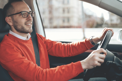 Man in a red shirt and glasses driving a car.
