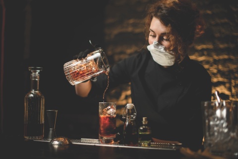 bartender pouring cocktail while wearing a mask and gloves to protect herself from COVID-19