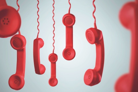 Red phone receivers hanging upside-down by the cord.