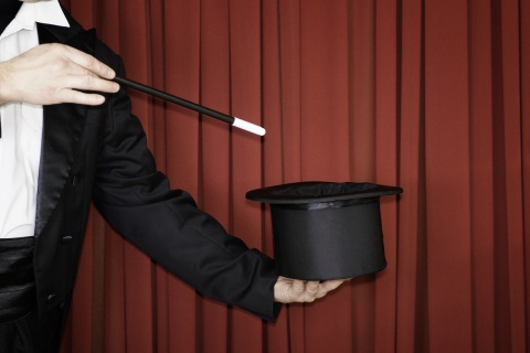 A magician pointing with a want to an empty top hat.