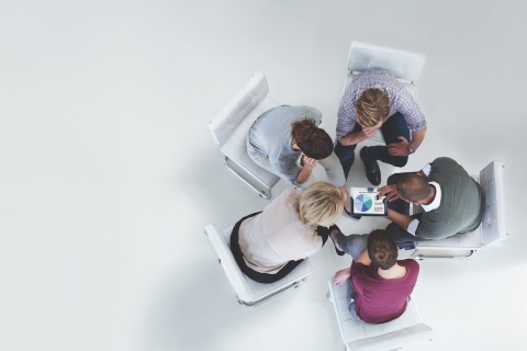 A group of independent insurance agents huddled around a tablet reviewing charts on the screen.