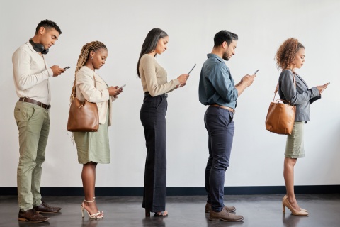 A group of young professionals, symbolizing independent agents, stand in line using smartphones in a modern office, reflecting the importance of agency perpetuation plans and identifying diverse funding sources for future business growth.