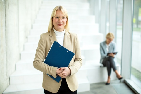 Image of a young businesswoman confidently standing with a file folder, symbolizing professionalism and organization. She exudes competence and assurance, embodying the concepts of life insurance aggregators and direct appointments in the financial industry.