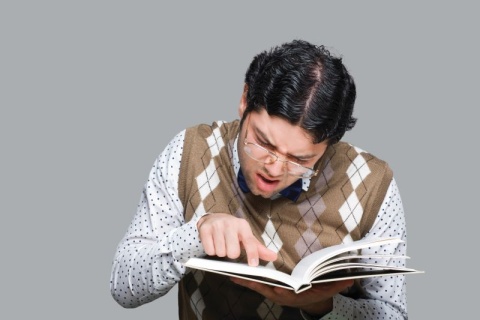 Man in sweater vest and glasses squinting and pointing at book