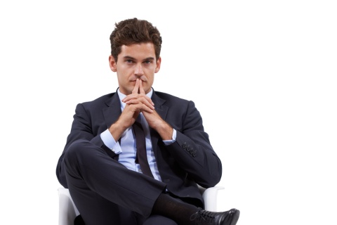 man wearing suit and tie, legs crossed while sitting in chair, hands on chin, thinking
