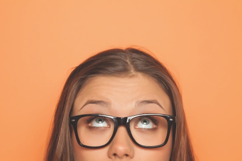 Woman with glasses looking up, on an orange background.