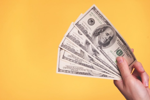 A fan of hundred-dollar bills against a yellow background.