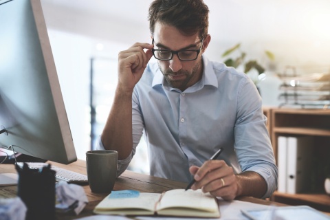 An independent insurance agent with glasses and a button-up shirt reviews notes in a planner.